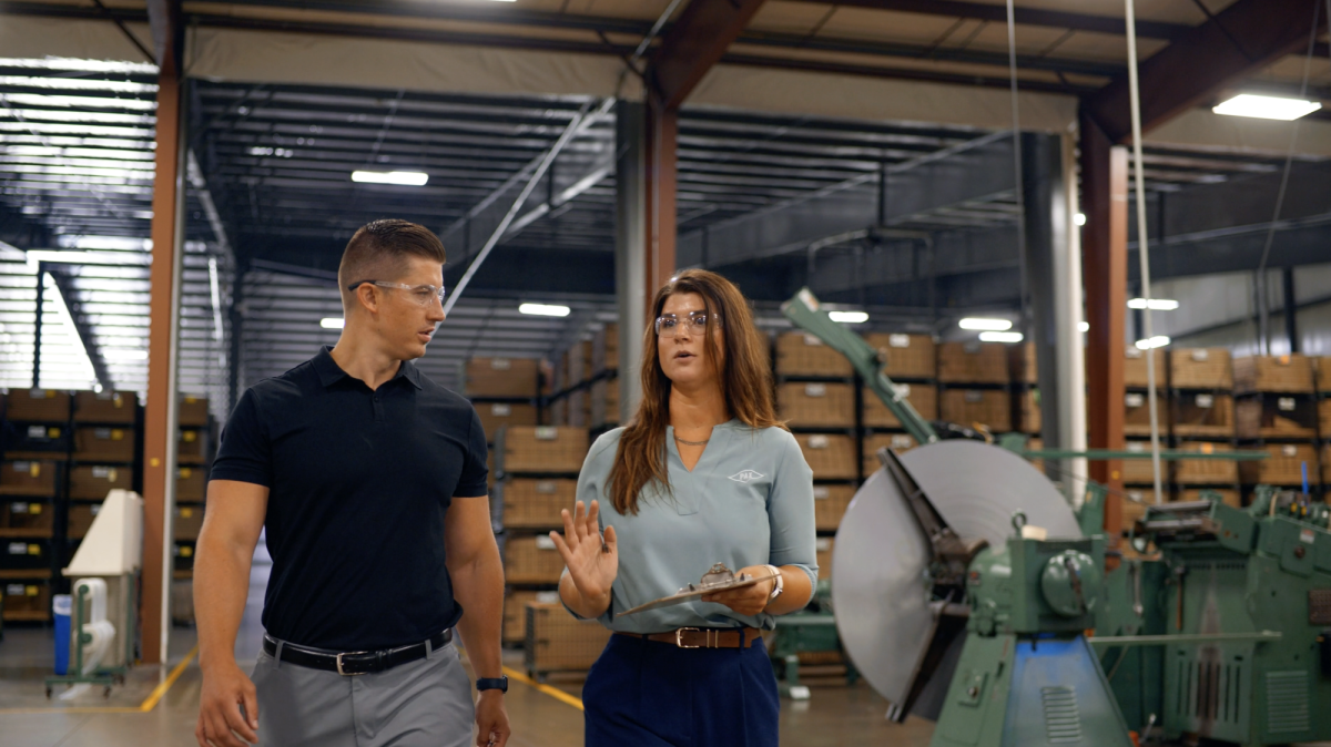 Mill Steel salesman and customer walk in a warehouse discussing coil quality.